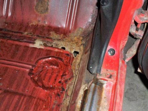1974 Pontiac Firebird - The interior floor pan of a red vehicle shows significant rust damage and a circular red material patch.