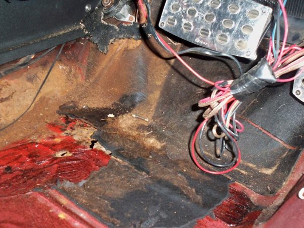 Car's floor pan is rusted out, with exposed wiring and pedals visible