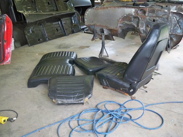 Car seats and floor pans laid out on a concrete floor next to a car chassis undergoing restoration