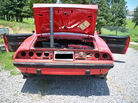 1974 Pontiac Firebird - The rear of a red car is shown with the trunk and driver's door open, revealing an empty interior and a large pipe.