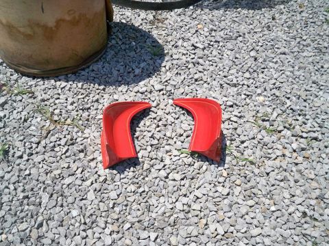 1974 Pontiac Firebird - Two red plastic fender flares are shown on a gravel surface, with a large cylindrical object in the background.