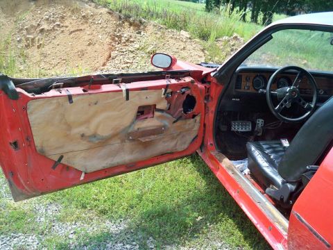 1974 Pontiac Firebird - The interior of a red car shows the driver's seat and dashboard with the door panel removed.