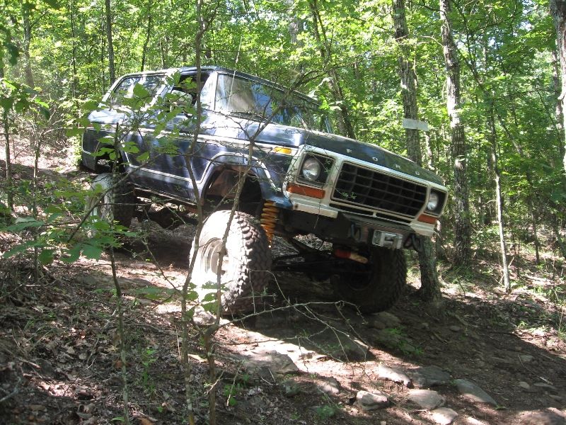Dark blue 1978 Ford Bronco off-roading on a rocky, wooded trail
