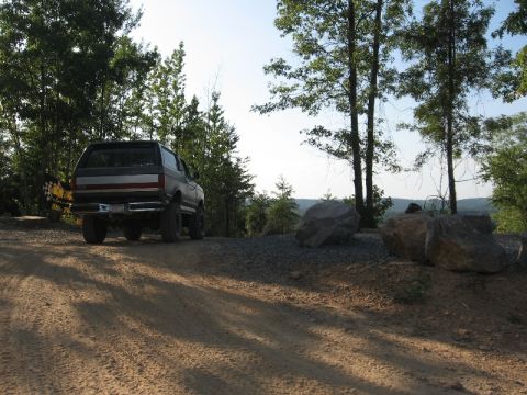 1978 Ford Bronco - Ford Bronco seen from the rear on a dirt road, surrounded by trees and large rocks.