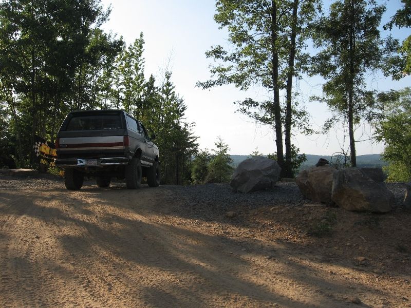 1980s Ford Bronco parked on a dirt road with trees and rocks in the background