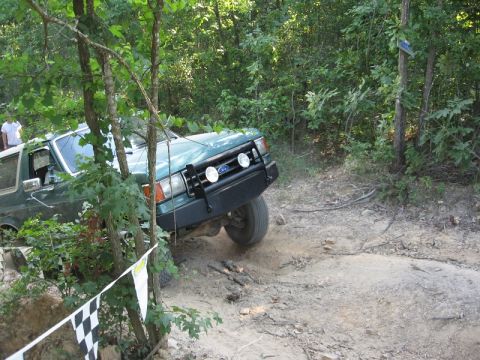 1978 Ford Bronco - A green Ford Bronco navigates a challenging off-road course surrounded by dense foliage.