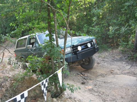 1978 Ford Bronco - A green SUV navigates a challenging off-road course, displaying a prominent aftermarket bumper and auxiliary lights.
