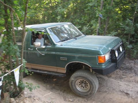 1978 Ford Bronco - Ford Bronco navigates an off-road course with trees and foliage visible.