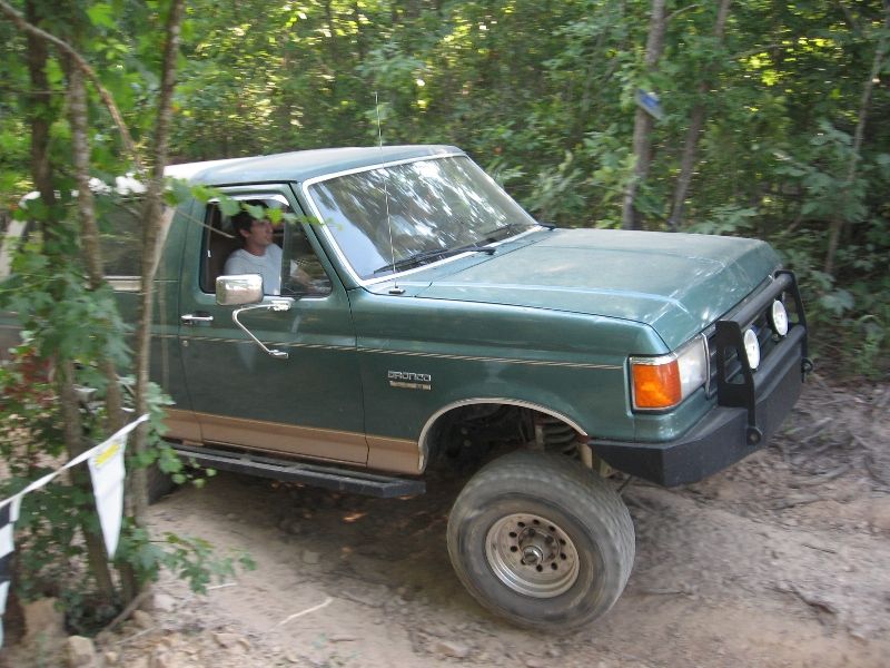 Green Ford Bronco with aftermarket bull bar and off-road tires on a dirt trail