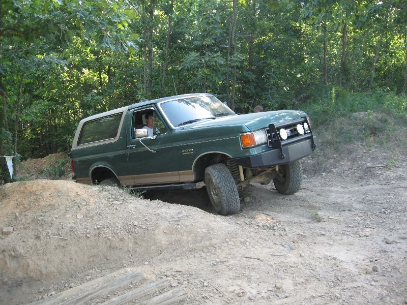 Green Ford Bronco driving over dirt mound on off-road trail. Has a brush guard on the front