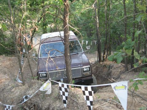 1978 Ford Bronco - A van drives through a wooded area with checkered flags marking a course.