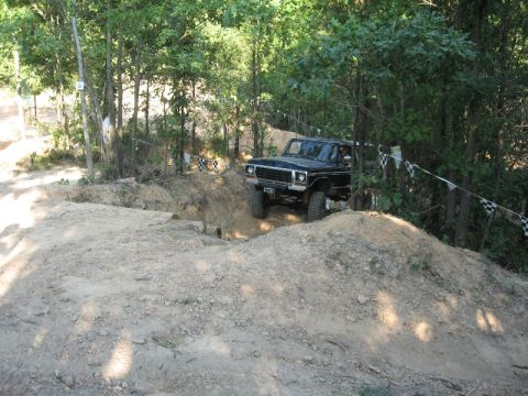 1978 Ford Bronco - This black SUV navigates a challenging dirt obstacle course surrounded by dense woods.