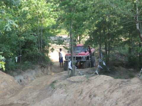 1978 Ford Bronco - A red 1978 Ford Bronco is parked on a dirt trail surrounded by trees, with a person standing nearby.