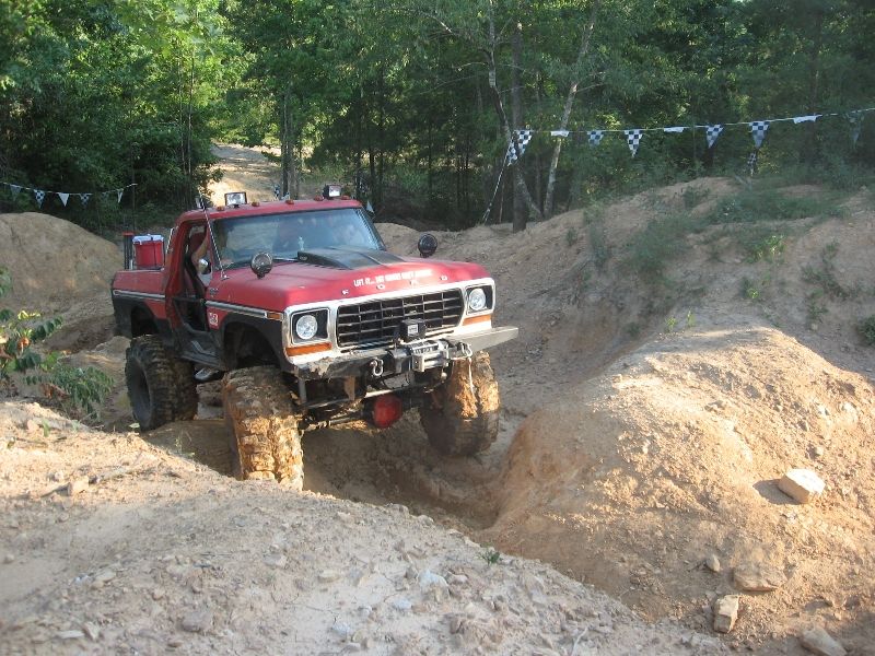 Red pickup truck with large tires navigating a dirt track, front grille visible
