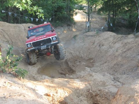 1978 Ford Bronco - A red 1978 Ford Bronco navigates a challenging off-road course with steep inclines and muddy terrain.