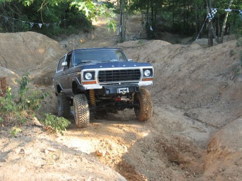 1978 Ford Bronco - This lifted 1978 Ford Bronco navigates a challenging dirt trail with checkered flags visible in the background.
