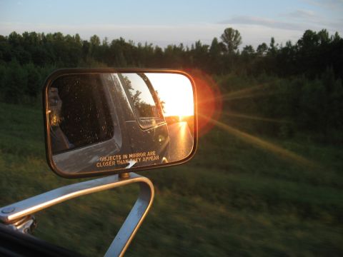 1978 Ford Bronco - Sunset viewed in a vehicle's side mirror while driving on a road.