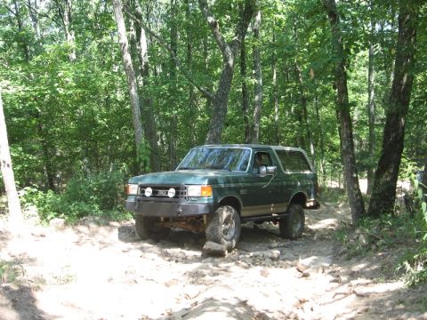 1978 Ford Bronco - This green SUV navigates a rocky, wooded trail, showing off its off-road capabilities. The vehicle's body style suggests a model from the l…
