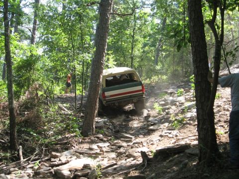 1978 Ford Bronco - A 1978 Ford Bronco navigates a challenging rocky trail through a wooded area.