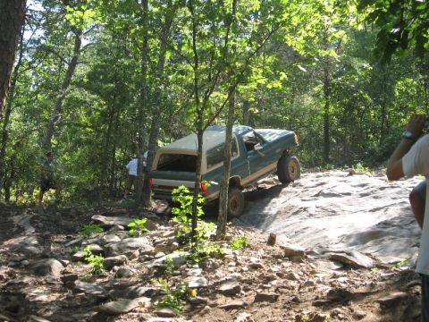 1978 Ford Bronco - A green 1978 Ford Bronco navigates a challenging rocky path through a wooded area.