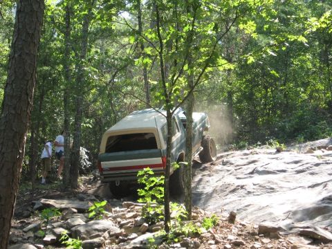 1978 Ford Bronco - Off-road vehicle navigates a challenging rocky path through a dense forest.