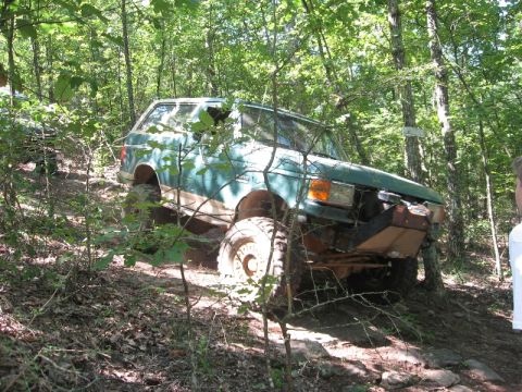 1978 Ford Bronco - A modified green SUV navigates a wooded trail with significant ground clearance.