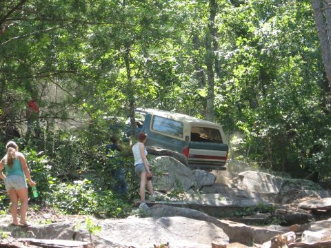 1978 Ford Bronco - A 1978 Ford Bronco navigates a challenging rocky path surrounded by dense trees.