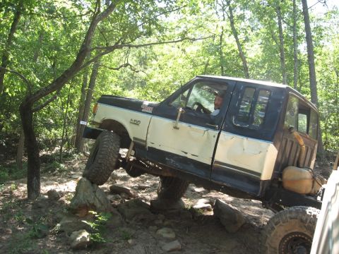 1978 Ford Bronco - A lifted Ford F-Series truck maneuvers over rocks on a wooded trail.