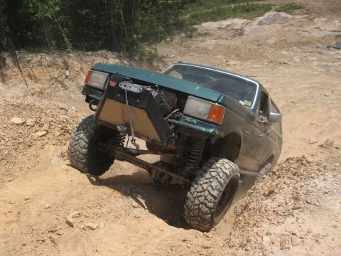 1978 Ford Bronco - This heavily modified SUV is navigating a challenging off-road terrain with steep inclines and loose dirt.