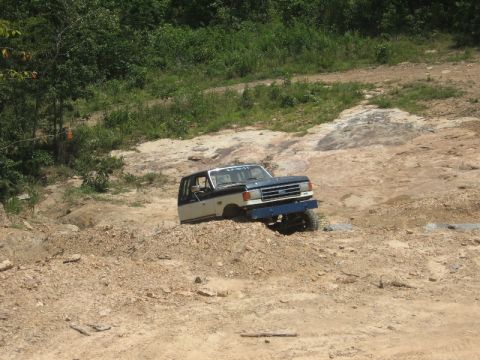 1978 Ford Bronco - Ford truck with two-tone paint is driving off-road on a dirt and rock path.