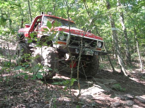 1978 Ford Bronco - This red off-road vehicle navigates a challenging rocky path through a wooded area.