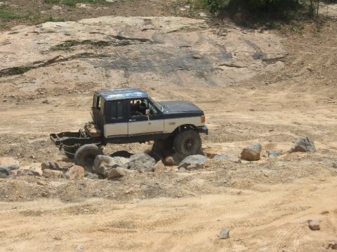 1978 Ford Bronco - Modified pickup truck with a shortened rear chassis drives over rocks on a dirt trail.