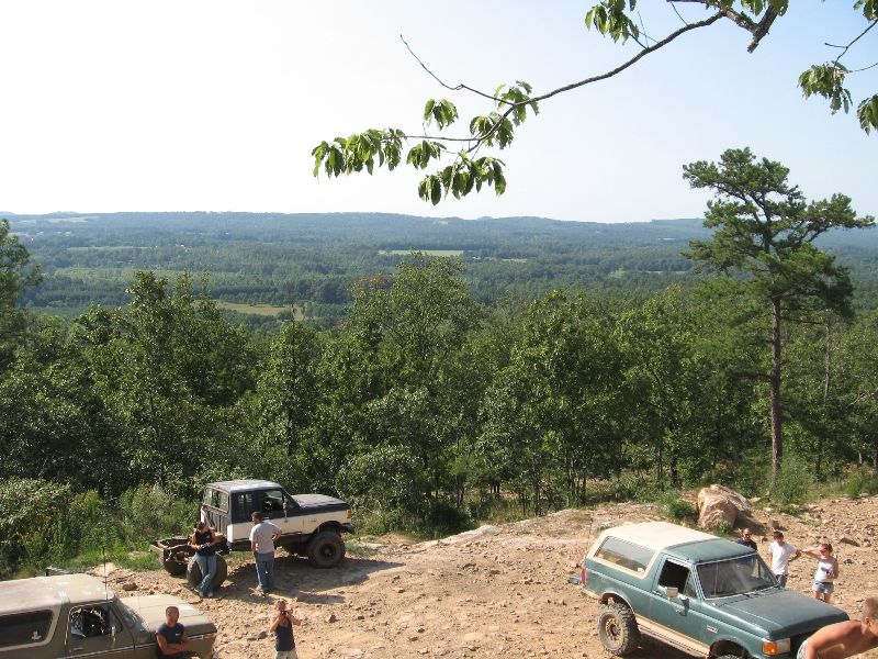 Several off-road vehicles parked on a dirt path with a vast forest and valley in the background