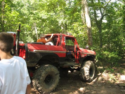 1978 Ford Bronco - A red 1978 Ford Bronco navigates a wooded trail with its doors removed.