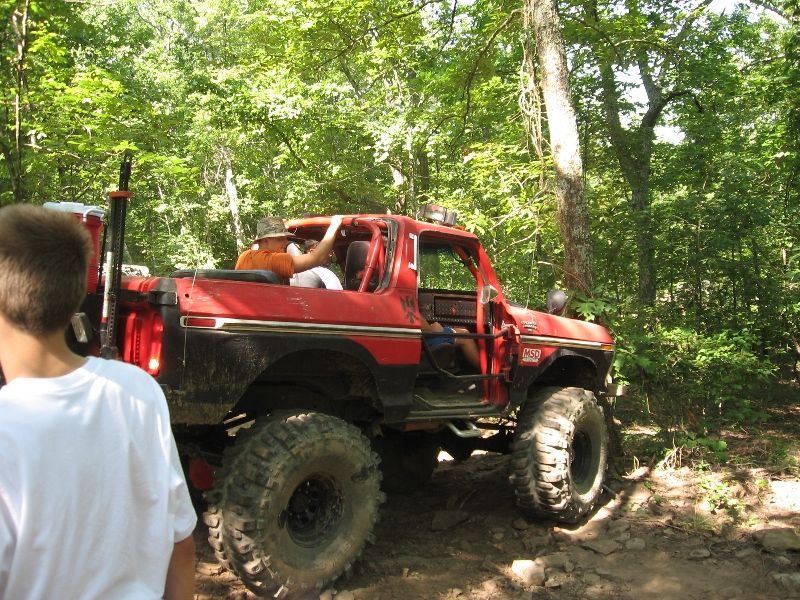 Red 1978 Ford Bronco with lifted suspension and large off-road tires driving on a dirt trail
