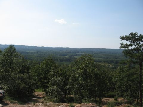 1978 Ford Bronco - Scenic overlook with dense forest and distant landscape under a bright sky. A vehicle is partially visible on the left.