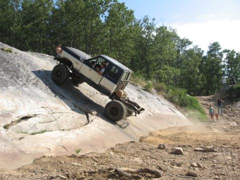 1978 Ford Bronco - Off-road vehicle navigates a challenging rocky incline, kicking up dust.