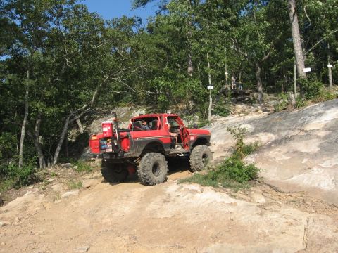 1978 Ford Bronco - A red 1978 Ford Bronco navigates a challenging off-road course with steep inclines and rocky terrain.