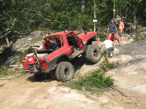 1978 Ford Bronco - A red 1978 Ford Bronco navigates a challenging rocky terrain with assistance from onlookers.