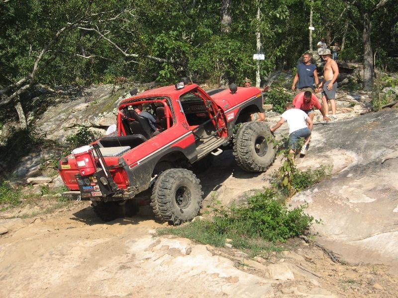 Red 1978 Ford Bronco off-roading on a rocky incline with people around