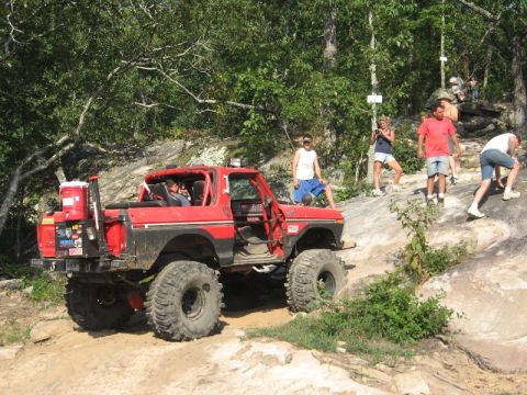 1978 Ford Bronco - A modified red 1978 Ford Bronco navigates a challenging rocky incline as onlookers observe the off-road adventure.