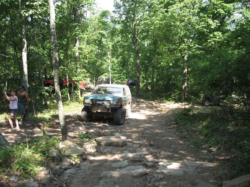 1978 Ford Bronco modified for off-roading on a rocky dirt trail with trees around