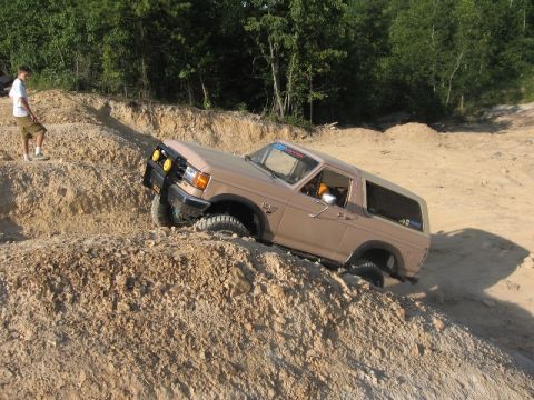 1978 Ford Bronco - A tan Ford Bronco navigates a steep dirt incline with its front right wheel elevated.
