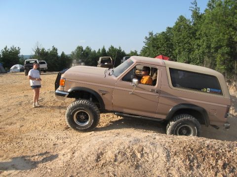 1978 Ford Bronco - A tan Ford Bronco navigates a dirt hill during an off-road excursion, with other vehicles and tents visible in the background.