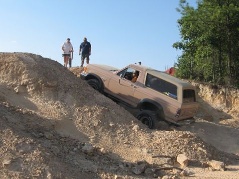 1978 Ford Bronco - Tan Ford Bronco full-size SUV descending a steep rocky bank at an off-road park, seen from the side with the driver visible through the ope…