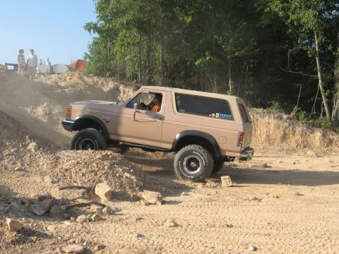 1978 Ford Bronco - A tan Ford Bronco navigates a steep, sandy incline with trees in the background.