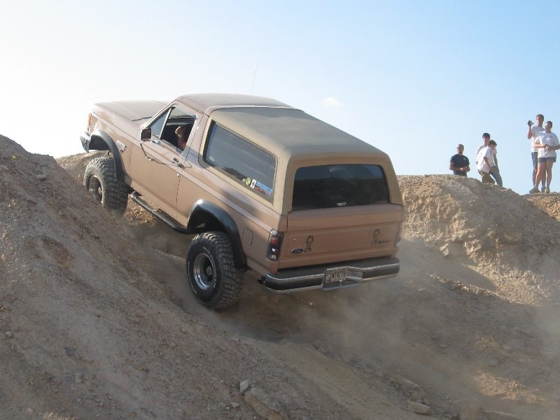 Tan Ford Bronco flexing on a dirt hill at an off-road park with spectators watching
