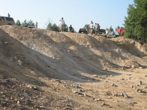 1978 Ford Bronco - A rutted dirt and rock hill climb at an off-road park, with spectators standing along the ridge above beside parked trucks and a red pop-up…