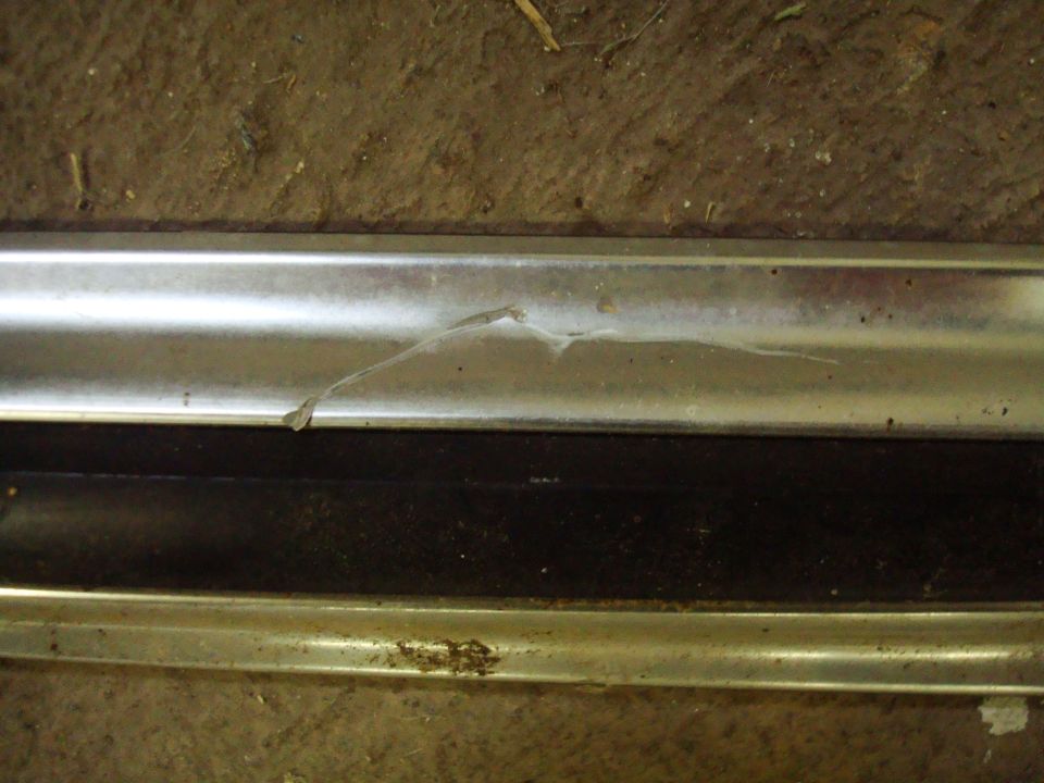 Creased and scratched chrome belt molding with rust, lying on a concrete floor