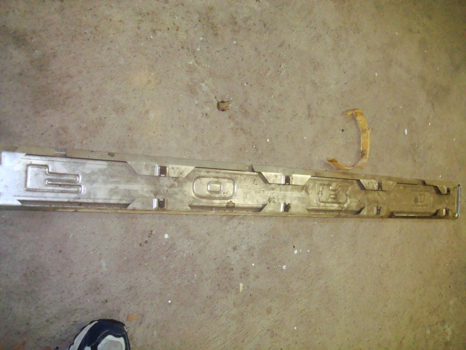 Metal trim piece with embossed letters, lying on a concrete floor
